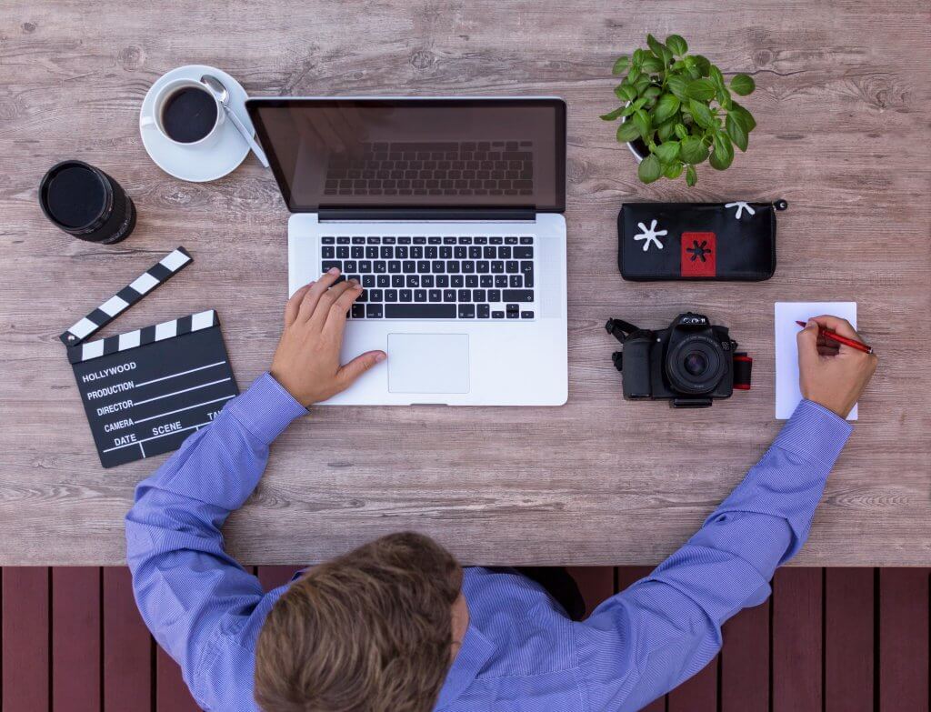 un homme qui écrit sur un pc avec une caméra et un café